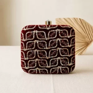 Clutiva regal maroon velvet square party clutch for women with gold leaf sequin embroidery standing on a cream surface.