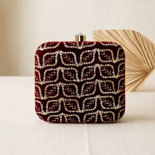 Clutiva regal maroon velvet square party clutch for women with gold leaf sequin embroidery standing on a cream surface.