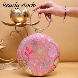 Clutiva Rose Aura round pink ethnic clutch featuring gold and pastel machine embroidery, a crystal-studded rhinestone circle handle, and traditional floral motifs.